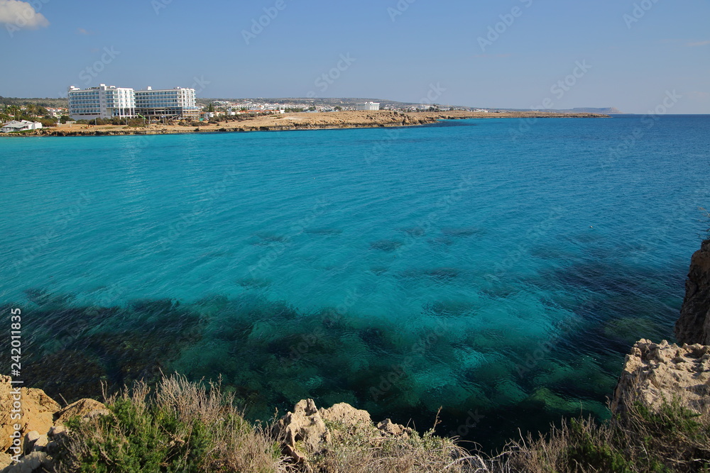 Beautiful coastline in Cyprus, bay, blue lagoon, clear water, rocky beach and hills on horizon, white architecture