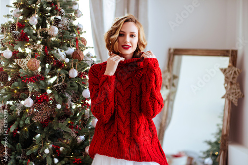 holidays, celebration and people concept - smiling woman in red sweater over christmas tree background © Margo Basarab