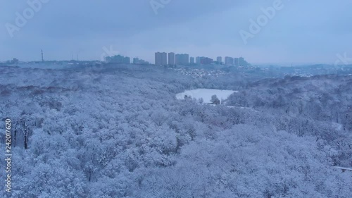 Beautiful city park covered with snow with appartment buildings in the background, aerial footage.