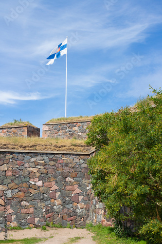 Granite walls of the historic fort Suomenlin Sveaborg in Finland on a summer day and the flag of Finland on fortifications.