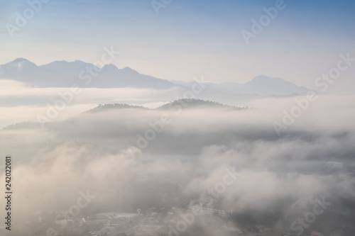 Top view misty morning above Mae Hong Son City, view of the sea of mist moving above city around with mountain and cloudy sky background, sunrise at Wat Phra That Doi Kong Mu, Mae Hong Son Thailand. © Yuttana Joe
