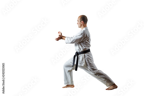 Adult male athlete performs formal karate exercises on a white isolated background