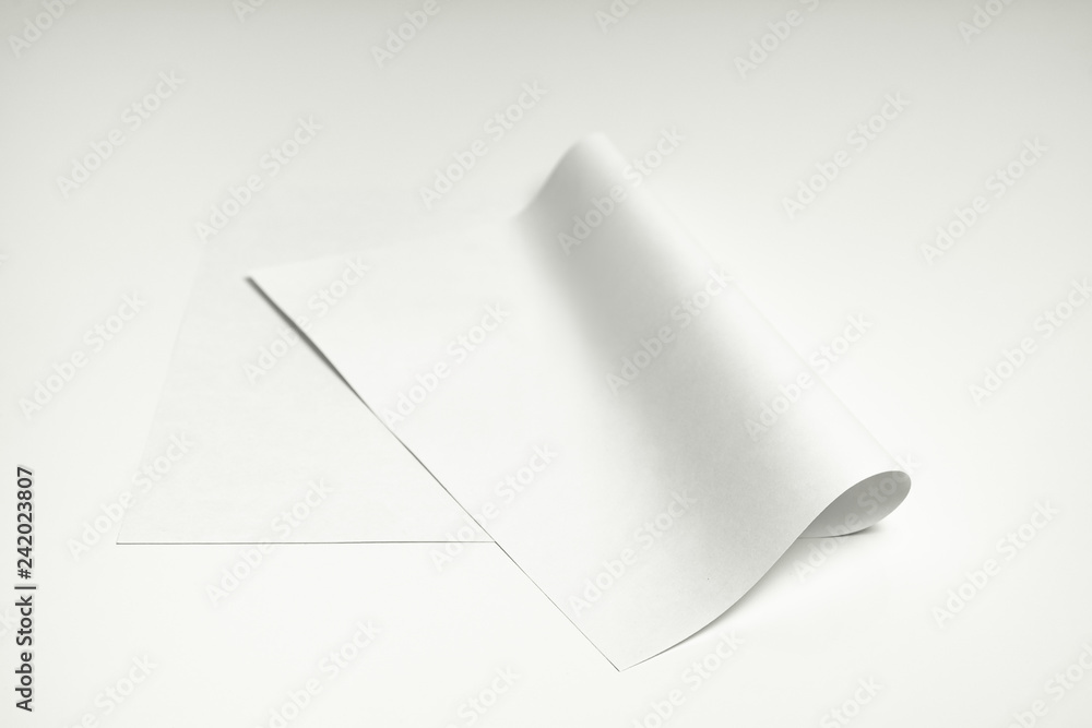 Blank paper sheet on white background. Close-up view of bent white paper laying on clean white table top Blank paper sheet on white background. Close-up view of bent white paper laying on clean white table top
