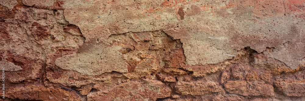 brick wall covered with old crumbling cement plaster with traces of paint.