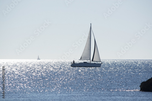 Backlit sailboat on bright and sunny sea with horizon