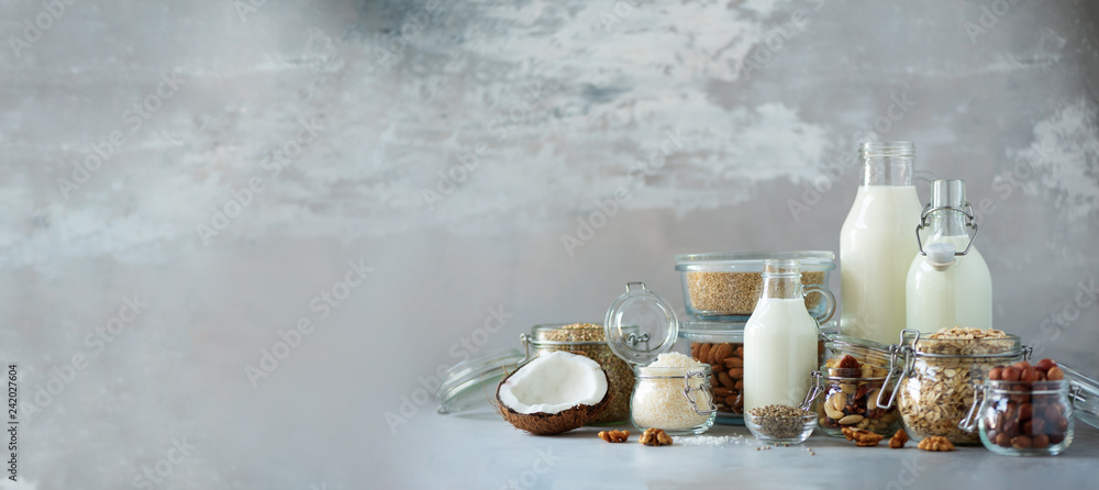 Φωτογραφία Glass bottles of vegan plant milk and almonds, nuts, coconut, hemp seed milk on grey concrete background