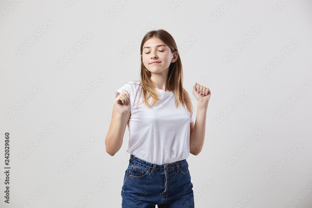 Calm and happy girl dressed in a white t-shirt and jeans is on a white background in the studio - obrazy, fototapety, plakaty 