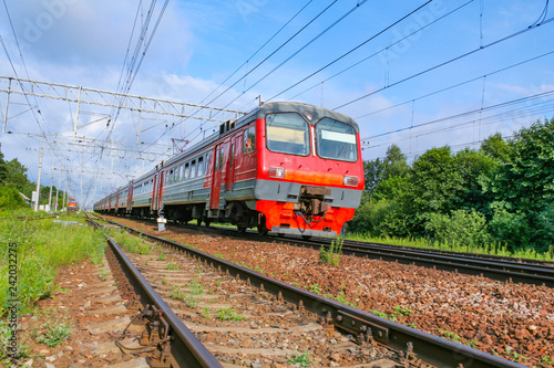 Bottom view on the approaching passenger electric train against a blue sky and green forest