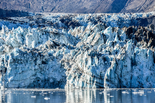 Crevasses, seracs and other detail features of the Johns Hopkins Glacier in Alaska with small pieces of glacial ice floating in ocean.