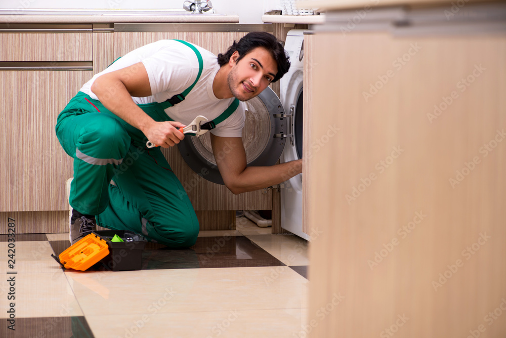 Young contractor repairing washing machine in kitchen Young contractor repairing washing machine in kitchen