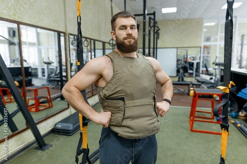 Portrait muscular caucasian bearded adult man in gym, dressed in bulletproof armored vest, military sport