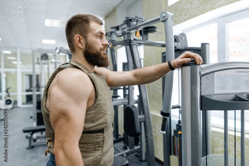 Portrait muscular caucasian bearded adult man in gym, dressed in bulletproof armored vest, military sport