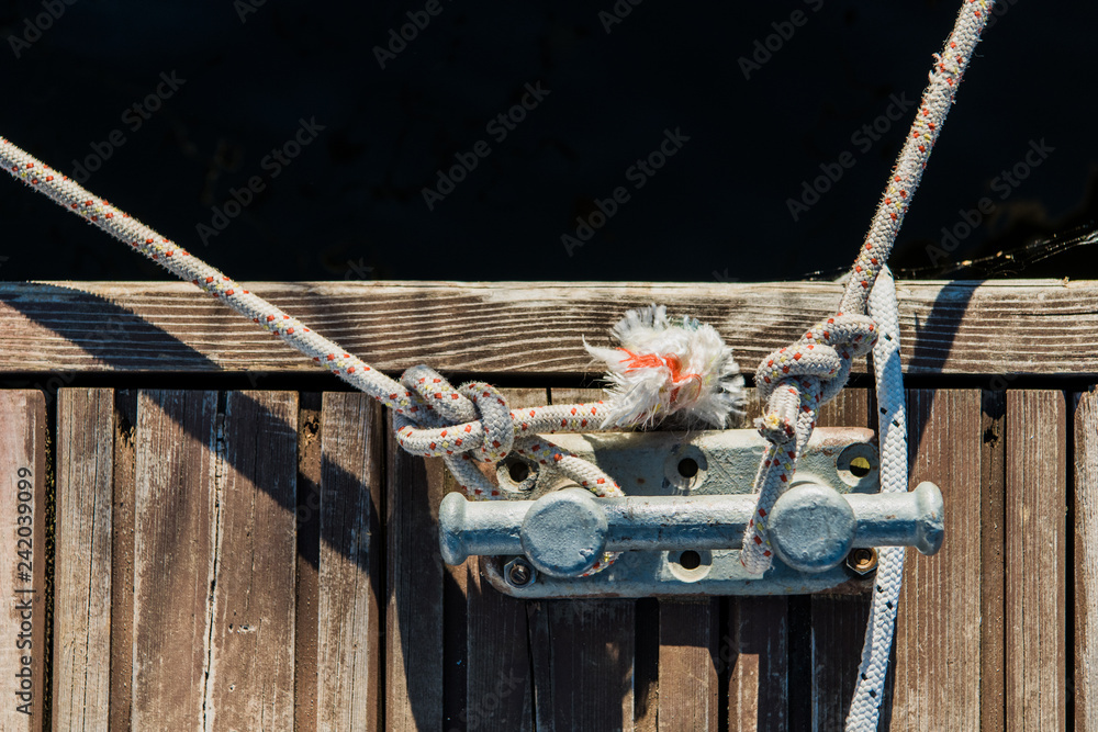 Naklejka premium Yachting detail, rope and mooring double cross bollard on bridge in port of sailing. Wooden pier