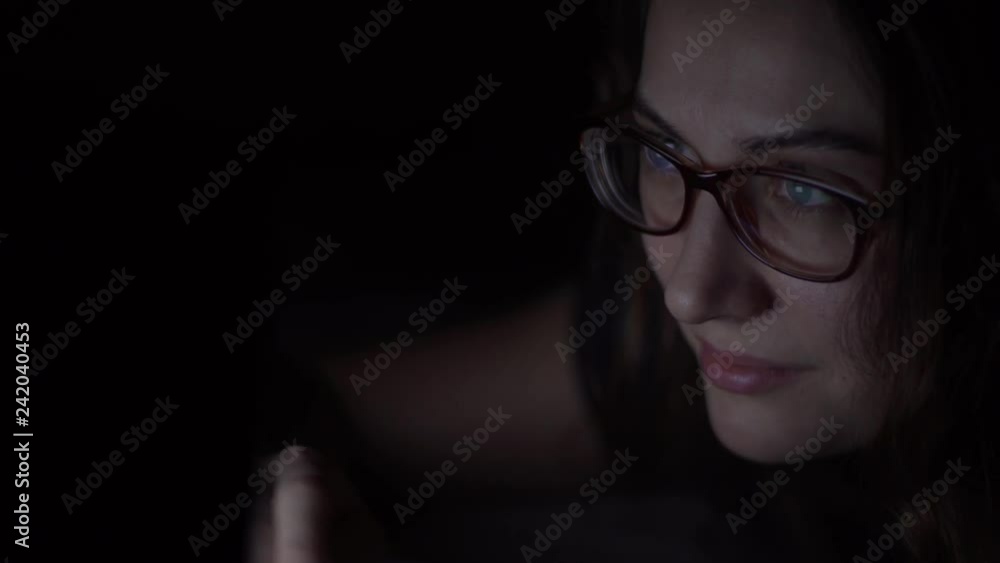 The girl in glasses uses a laptop lying on the bed at night. Isolated light The girl in glasses uses a laptop lying on the bed at night. Isolated light