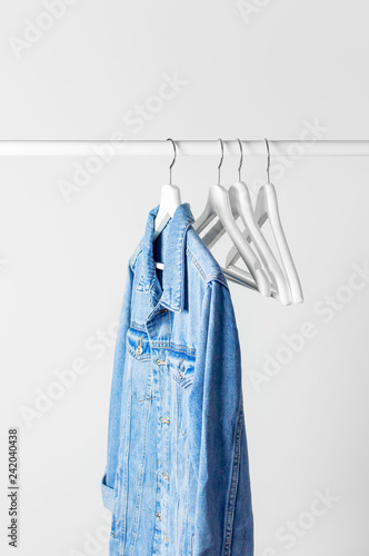 Blue denim jacket on white wooden coat hanger on a rod against light gray wall flat lay copy space. Denim, fashionable jacket, women's or men's trend clothing, fashion background. Store concept, sale. © olgaarkhipenko