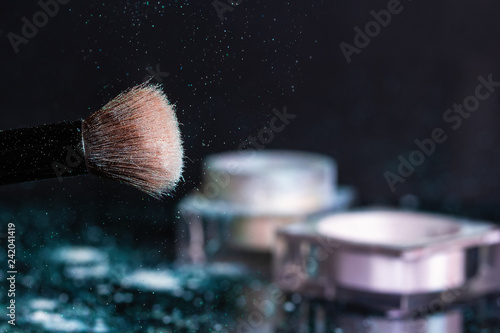 White-blue shadows, glitter on the cosmetic brush and a jar with a lid on a dark background