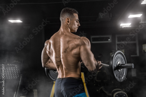 Young handsome sexy man, athlete, bodybuilder, weightlifter, in a modern gym is covered with a dark background, doing exercises for the biceps using sporting goods - weights. 