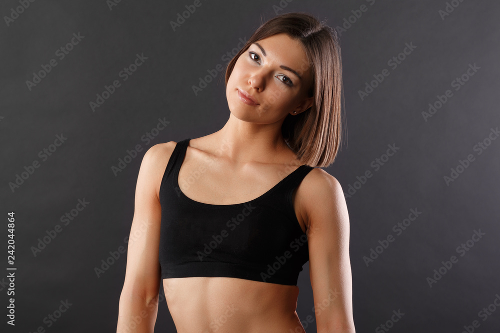 Obraz premium horizontal Studio half-length portrait of a beautiful girl in excellent physical shape, sportswear, uniform dark background