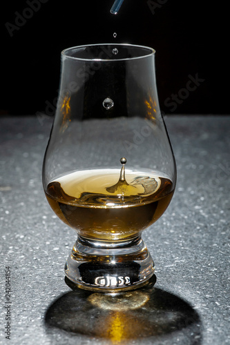 Drops of water being added to a glass of whisky, dark surface and background