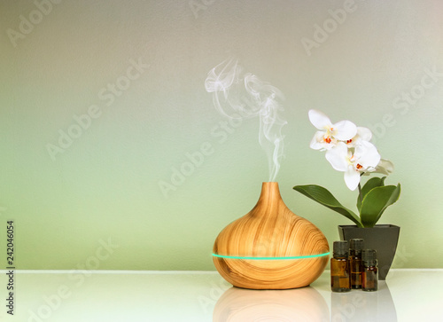 Electric Essential oils Aroma diffuser, oil bottles and flowers on green gradient surface with reflection
