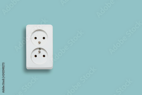 White electric socket on blue pastel background. The concept of electric power consumption, use of electricity. Savings on energy supply, power supply of various household items. Minimalist photo.