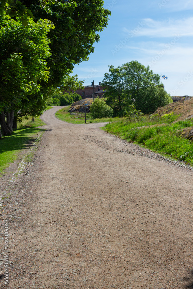 Country road, trees and old buildings are part of the natural Finnish landscape on Suomenlinna Island in Finland on a summer day.