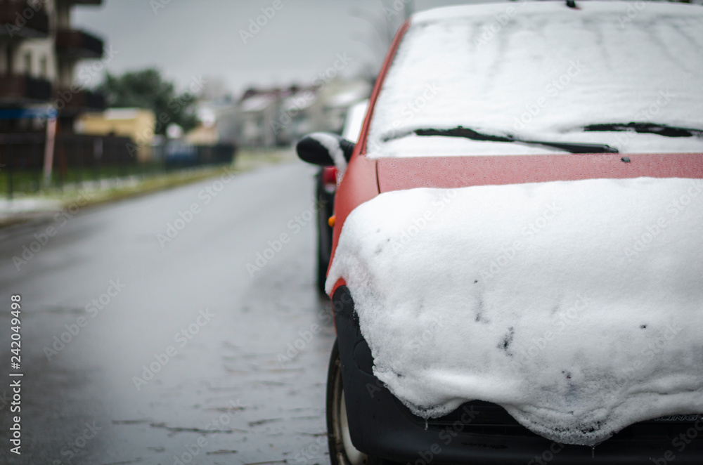Obraz premium Red car covered with snow along the road. Concept of winter, snowfall