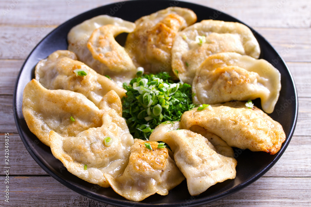 Fried dumplings stuffed with meat and served with chopped parsley and spring onion on a black plate on a wooden rustic table
