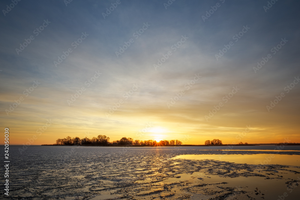 Winter landscape with frozen river and sunset fiery sky.