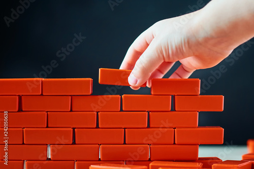 Hand puts last brick on wall. Concept of construction and building
