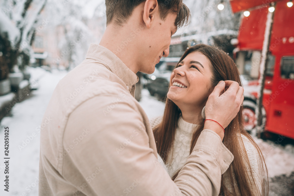 young guy and beautiful girl kiss in a snowy park. Couple in sweaters.