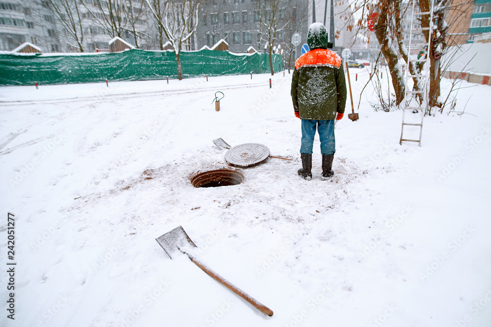 Sewer workers with shovel open manhole blockage during snowfall. Sewerage worker on street cleaning pipe. Mounting of  fiber optical system in  winter in blizzard and ice. Open manhole of  city sewer