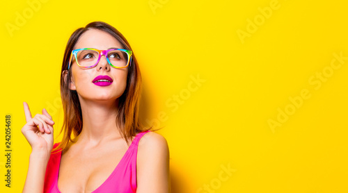 Young girl in pink one-piece swimming suit with eyeglasses on yellow background