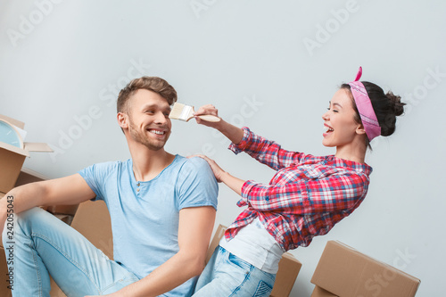 Obraz na plátně Young couple moving to new place man sitting on box looking at woman teasing him