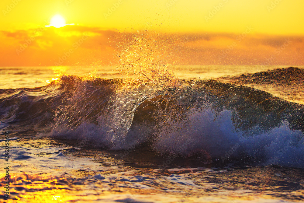 Fototapeta premium Złoty wschód słońca i rozpryskiwania niebieskie fale morza w pobliżu plaży