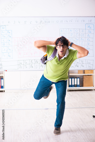 Young male student chemist in front of periodic table 