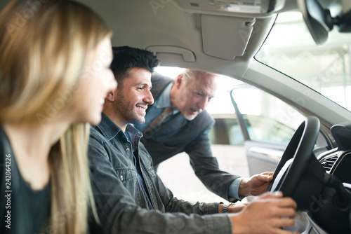 Foto Happy young family talking to the salesman and choosing their new car in a showr