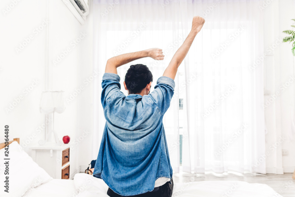 Man sitting near the window and stretching in bed after wake up.man happy and relaxed breathing fresh air at morning Man sitting near the window and stretching in bed after wake up.man happy and relaxed breathing fresh air at morning