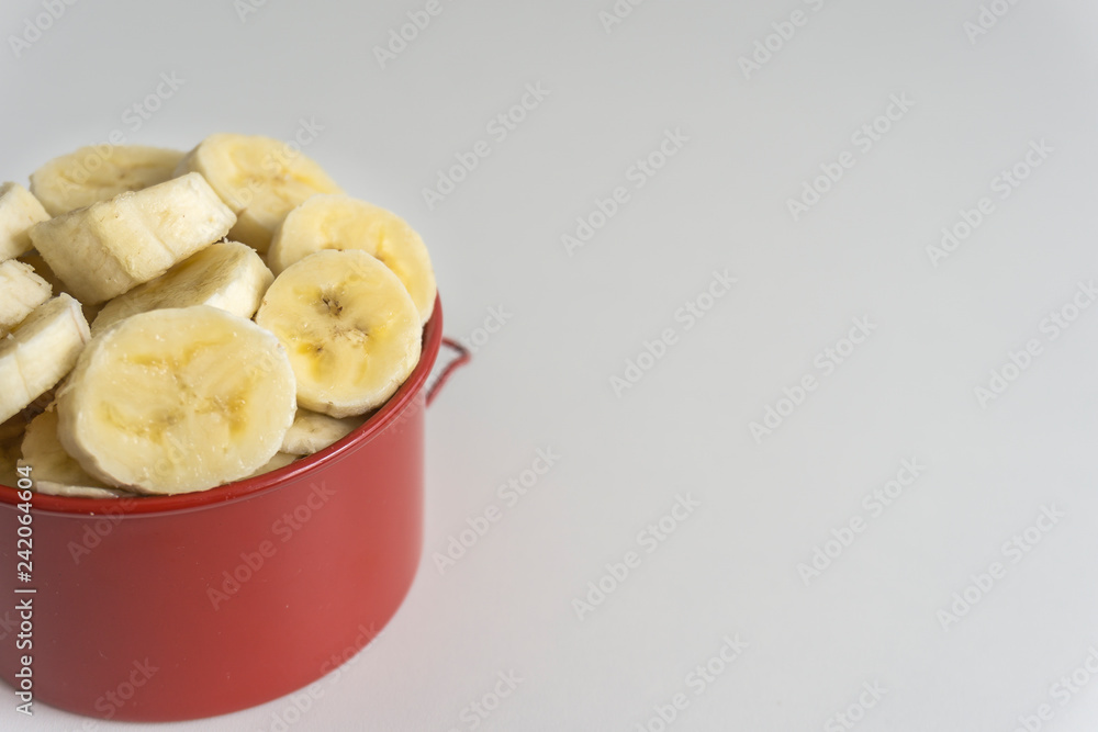 Red bowl with banana slices on white background. Red bowl with banana slices on white background.