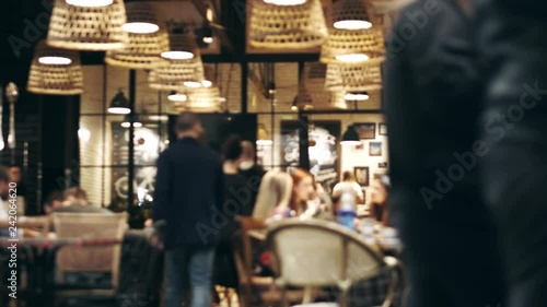 Blurred picture of the interior of a large beautiful restaurant with bright lighting. The waitress comes to the table and gives the visitors a menu and goes for drinks. Defocused restaurant photo
