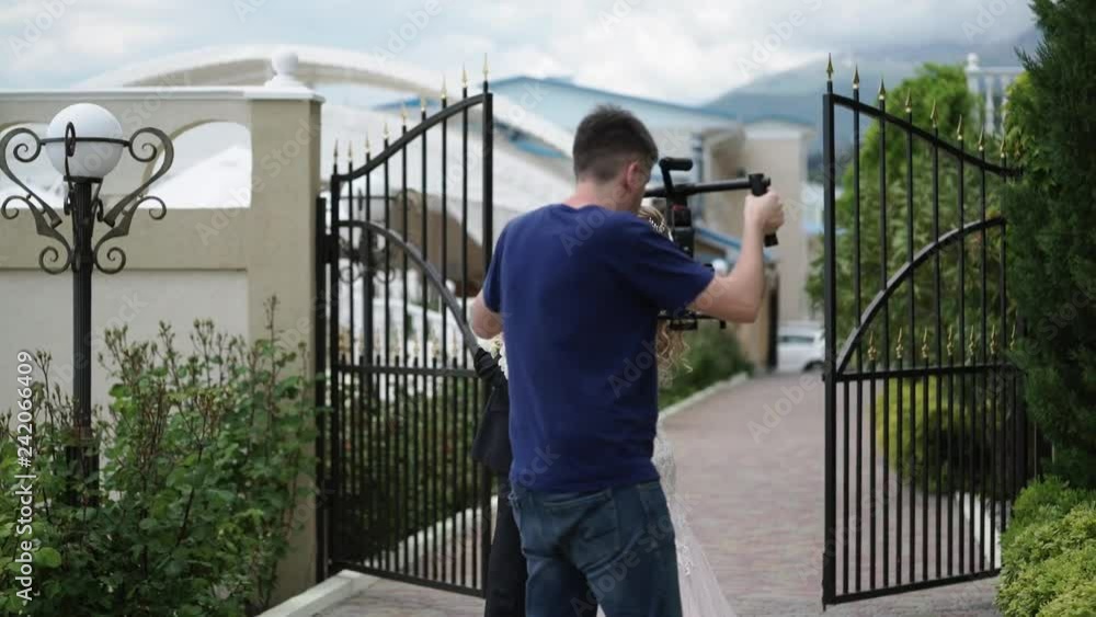 Videograph shooting video with steadicam. Young beautiful bride in a wedding dress goes to the groom. Meeting of the newlyweds outdoors Videograph shooting video with steadicam. Young beautiful bride in a wedding dress goes to the groom. Meeting of the newlyweds outdoors