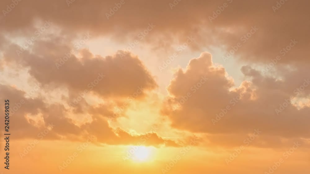 Timelapse of heavenly fluffy yellow and orange sunset clouds billowing past as the sun slowly drops toward the horizon, with brief glimpses of blue sky behind Timelapse of heavenly fluffy yellow and orange sunset clouds billowing past as the sun slowly drops toward the horizon, with brief glimpses of blue sky behind