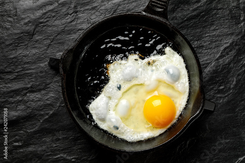 Fried egg on a black cast-iron pan, top view