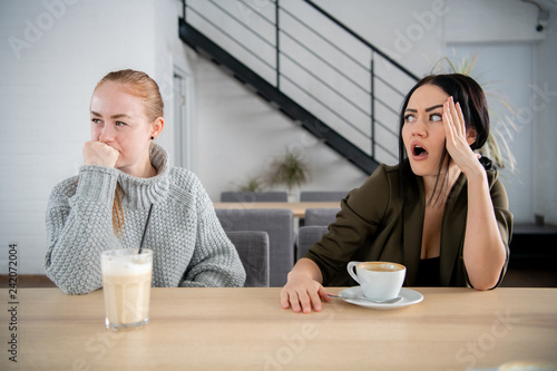 Two upset international girls offended at each other sadly looking aside spending time together in courtyard of cafe. Interracial relationship