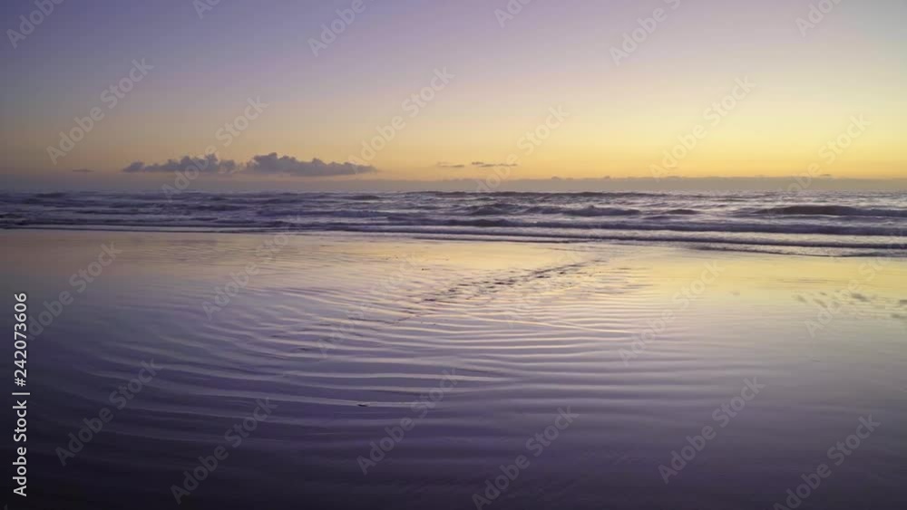 Metallic looking wet sand and ocean water reflect brilliant yellow and purple dusk sky colors as the tide rises at South Carlsbad State Beach, Calrsbad, California with waves in the distance Metallic looking wet sand and ocean water reflect brilliant yellow and purple dusk sky colors as the tide rises at South Carlsbad State Beach, Calrsbad, California with waves in the distance
