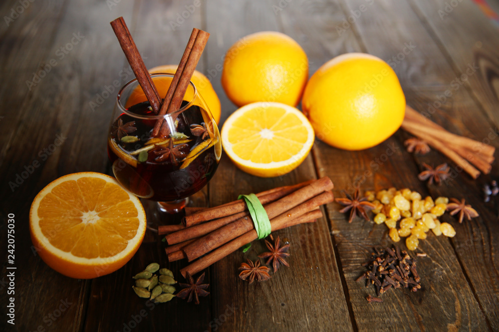 flavored mulled wine in a glass with two sticks of cinnamon and spices, with ingredients for it: cinnamon, anise, cardamom, pepper, oranges, almonds, raisins on a wooden background flavored mulled wine in a glass with two sticks of cinnamon and spices, with ingredients for it: cinnamon, anise, cardamom, pepper, oranges, almonds, raisins on a wooden background