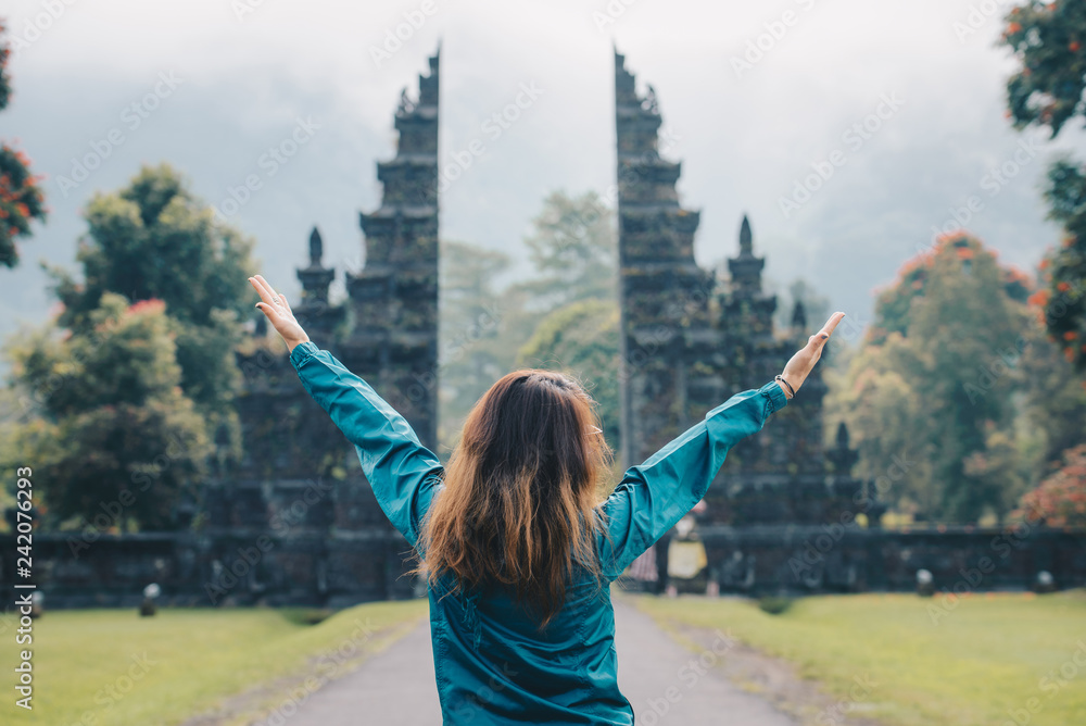 Back view of women enjoy her holiday and raise hands up in front of traditional Hindu gate in Bali island, Indonesia.