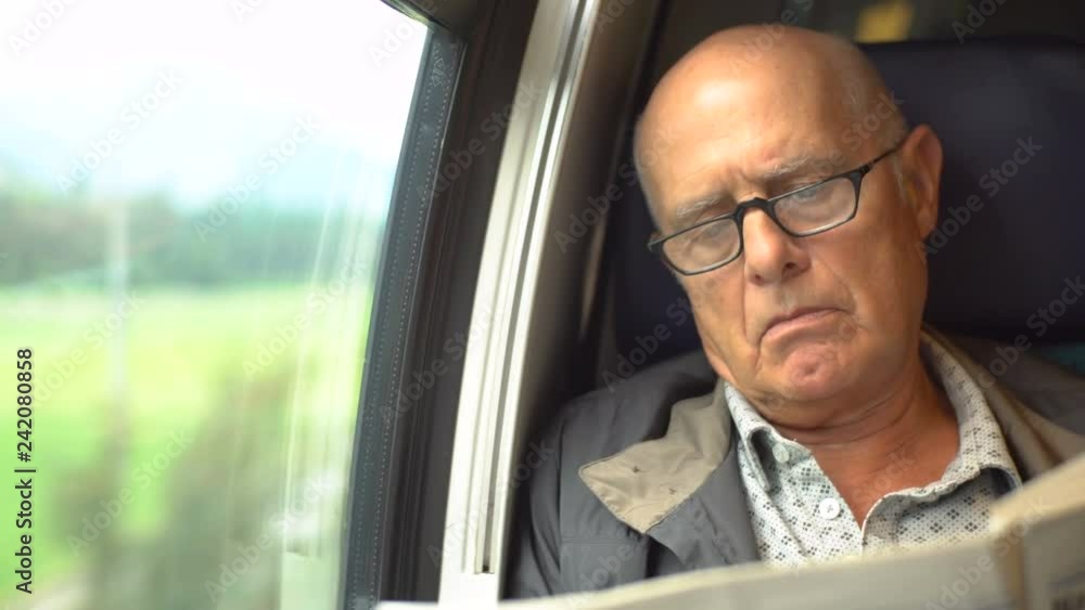 Elderly Commuter Reading Newspaper on Way to Work in Train Elderly Commuter Reading Newspaper on Way to Work in Train