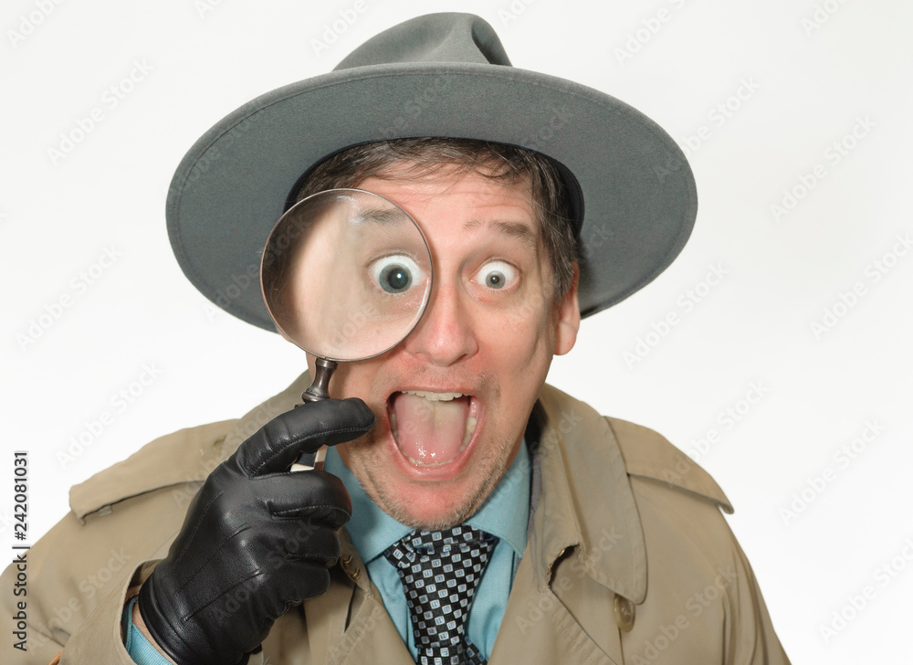 Detective man wearing a fedora holding a magnifying glass with a funny smile. Detective man wearing a fedora holding a magnifying glass with a funny smile.