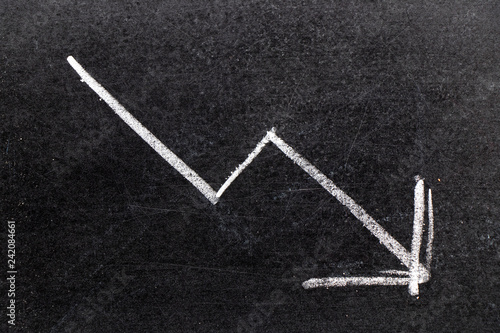 White chalk hand drawing in arrow down shape on black board background (Concept of stock decline, down trend of business, economy)